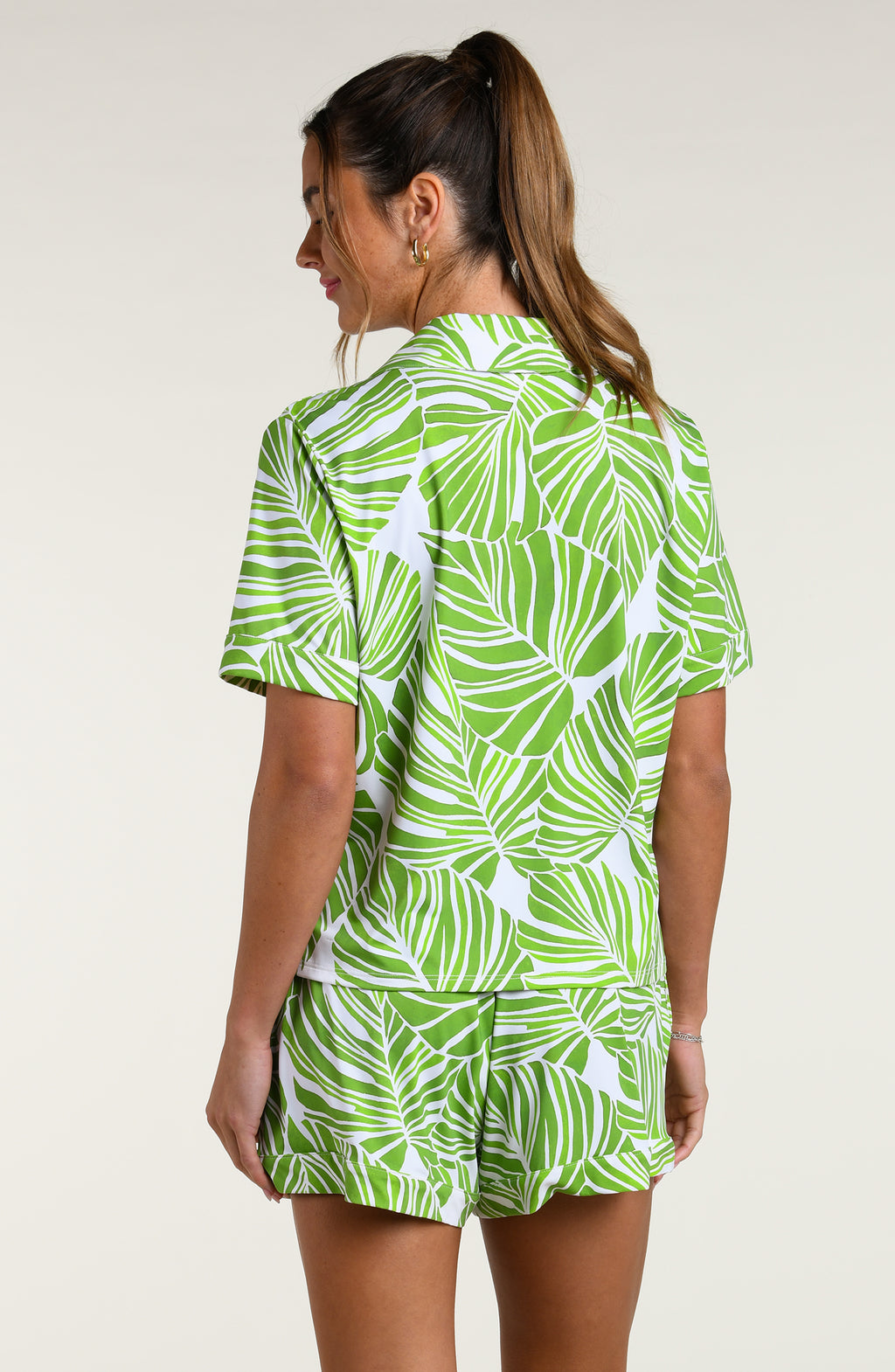 Woman wearing a green and white leaf-patterned pajama set against a plain white background.
