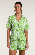 Woman wearing a green and white leaf-patterned pajama set against a plain white background.