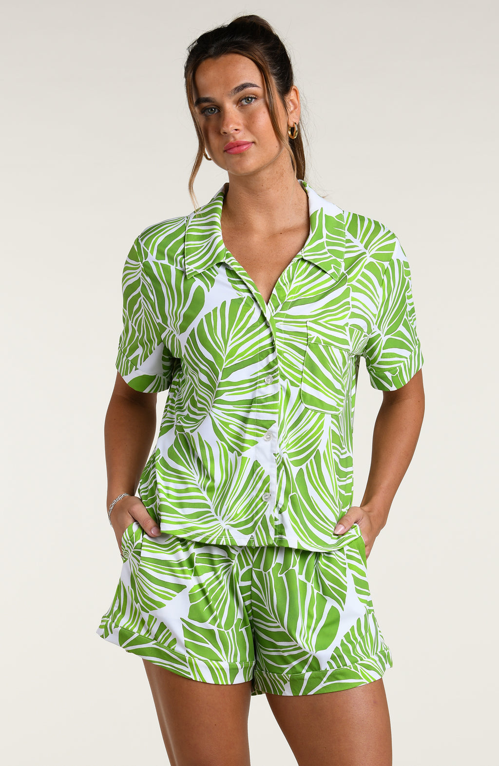 Woman wearing a green and white leaf-patterned pajama set against a plain white background.