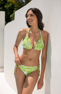 Woman wearing a green and white bikini top and matching bottom against a white wall.