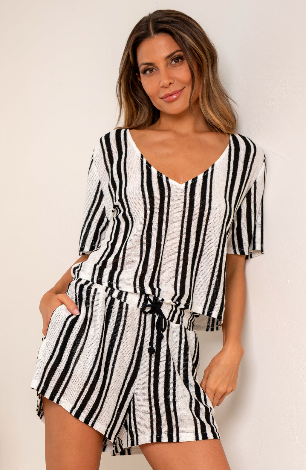 Woman wearing a black and white striped short sleeve top and matching shorts against a beige wall.