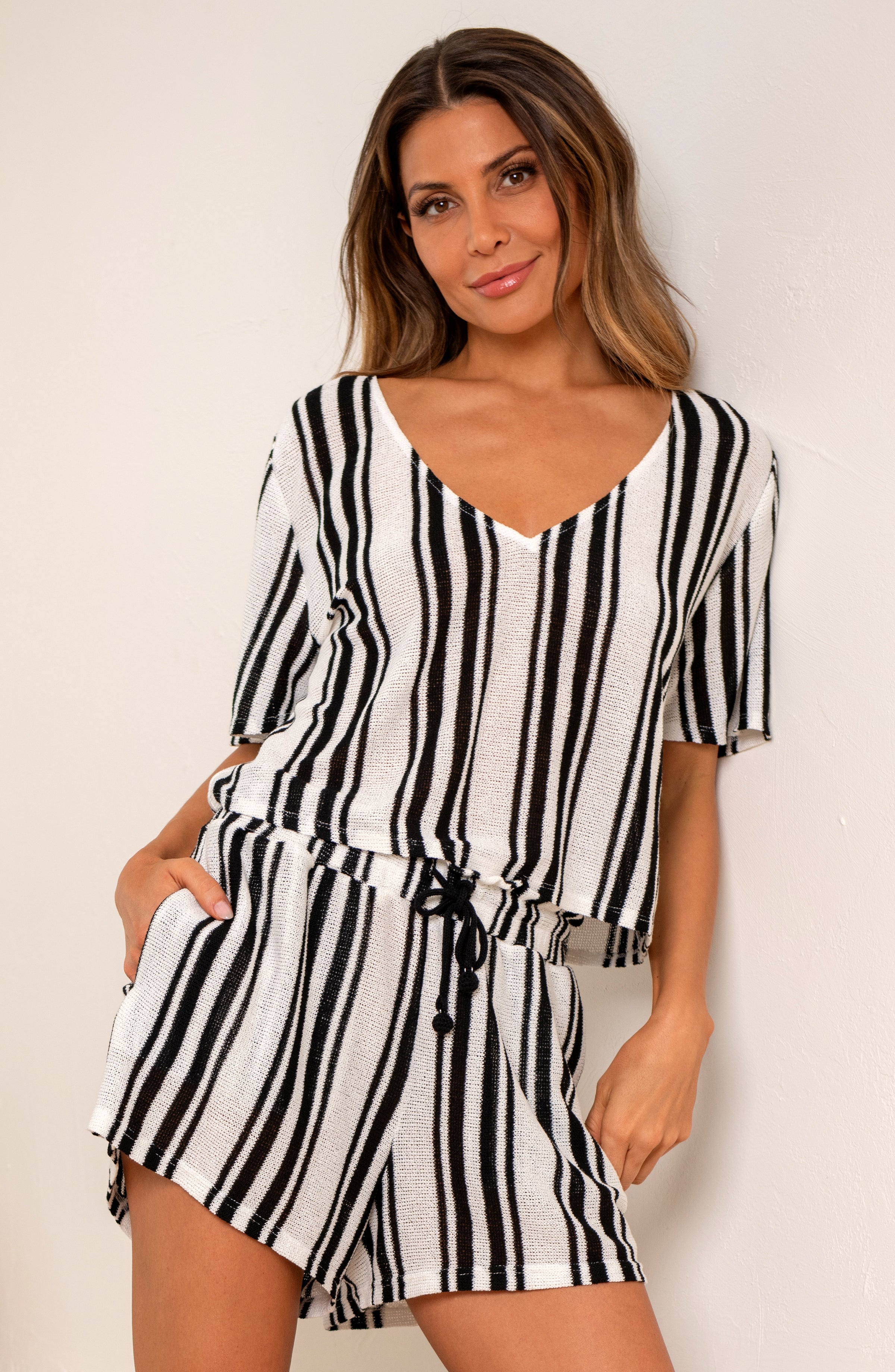 Woman wearing a black and white striped short sleeve top and matching shorts against a beige wall.