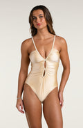 Woman wearing a champagne colored one piece swimsuit against a white background.