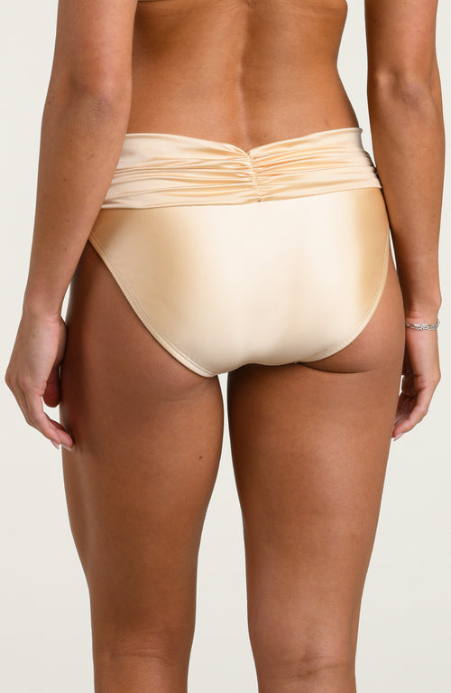 Woman wearing champagne colored bikini bottoms against a white background. 