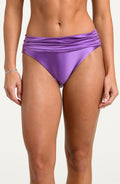 Woman wearing lavender colored bikini bottoms against a white background. 