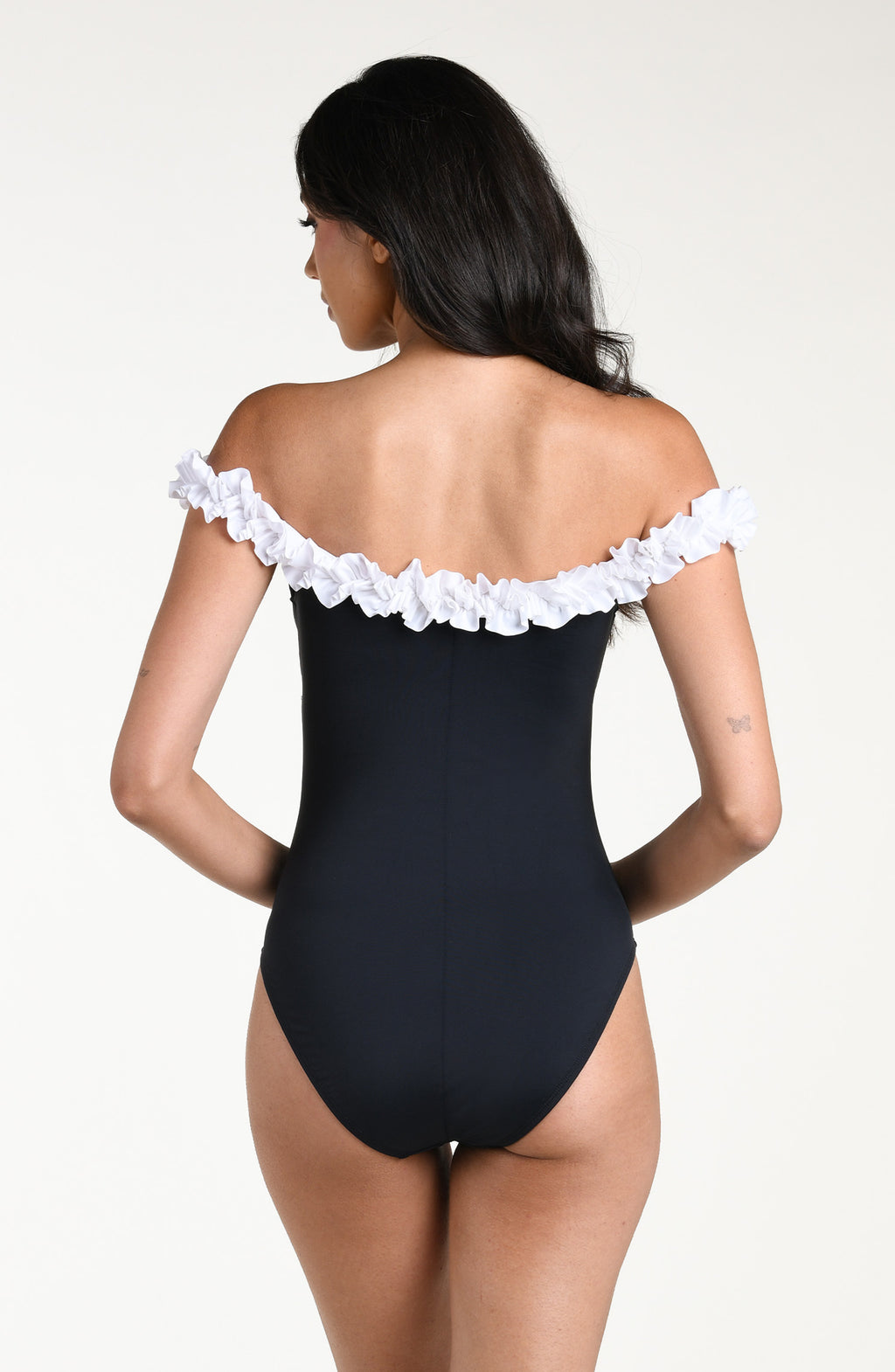 Woman wearing a black one-piece swimsuit with white ruffle details on a white background