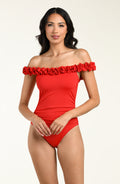 Woman wearing a red off-shoulder one piece swimsuit with floral details on a beige background