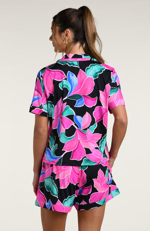 Woman wearing a colorful tropical patterned short sleeve top and shorts pajama set against a white background