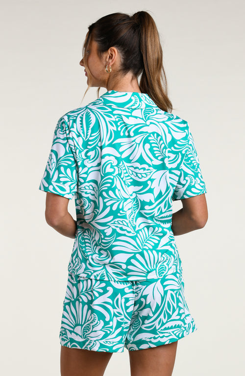 Woman wearing a teal and white patterned short sleeve shirt and shorts pajama set against a plain background