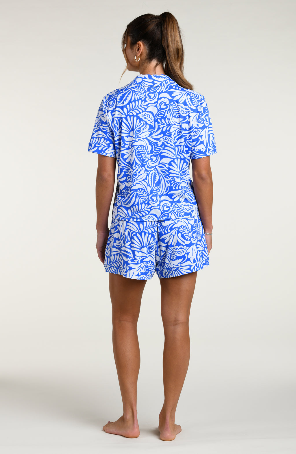 Woman wearing a blue and white patterned short sleeve shirt and shorts pajama set against a plain background