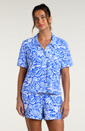 Woman wearing a blue and white patterned short sleeve shirt and shorts pajama set against a plain background