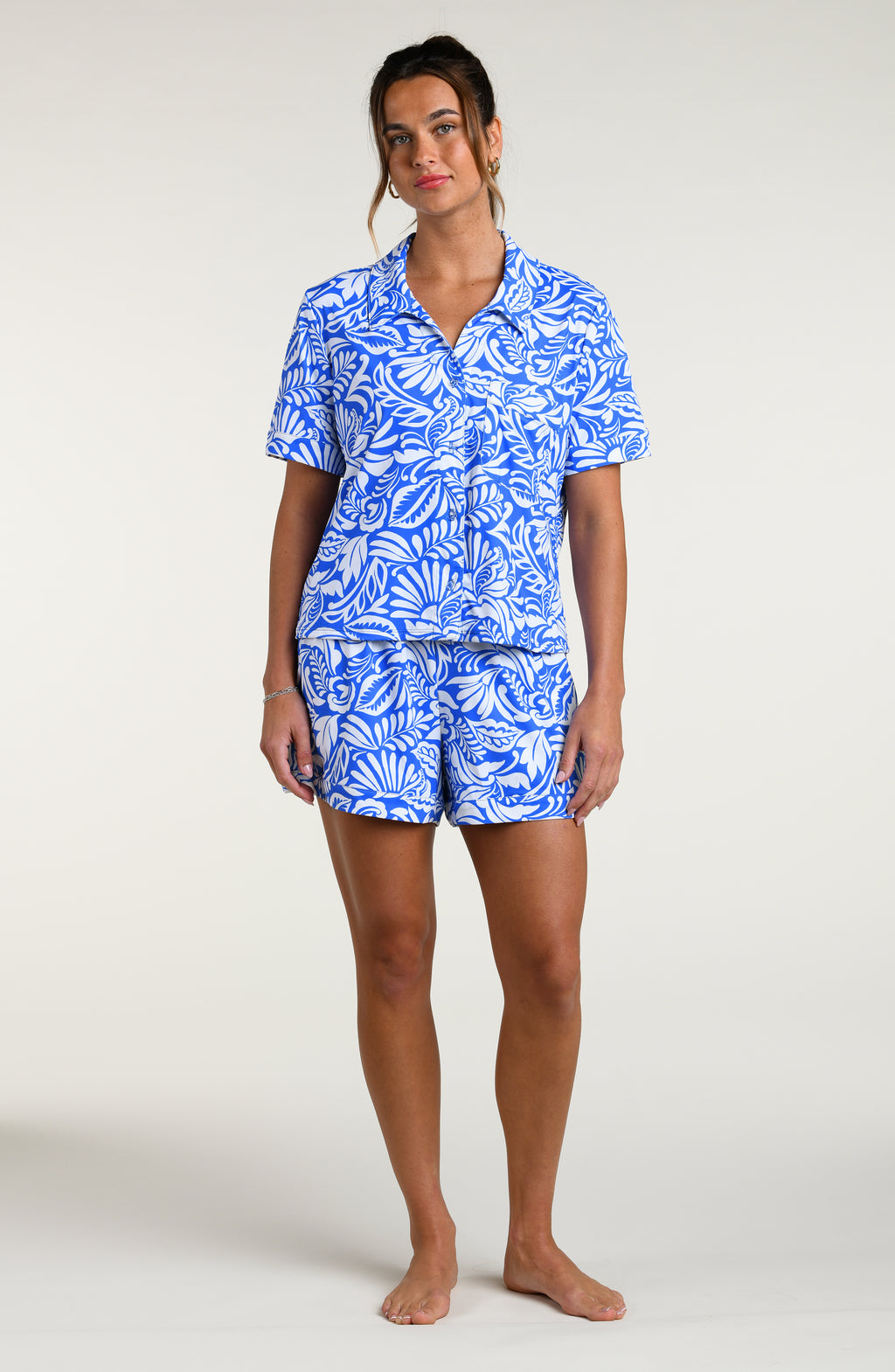 Woman wearing a blue and white patterned short sleeve shirt and shorts pajama set against a plain background