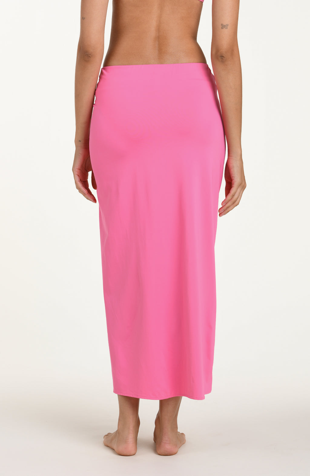 Back image of model wearing a rose pink colored maxi cover-up skirt with a high side slit. 