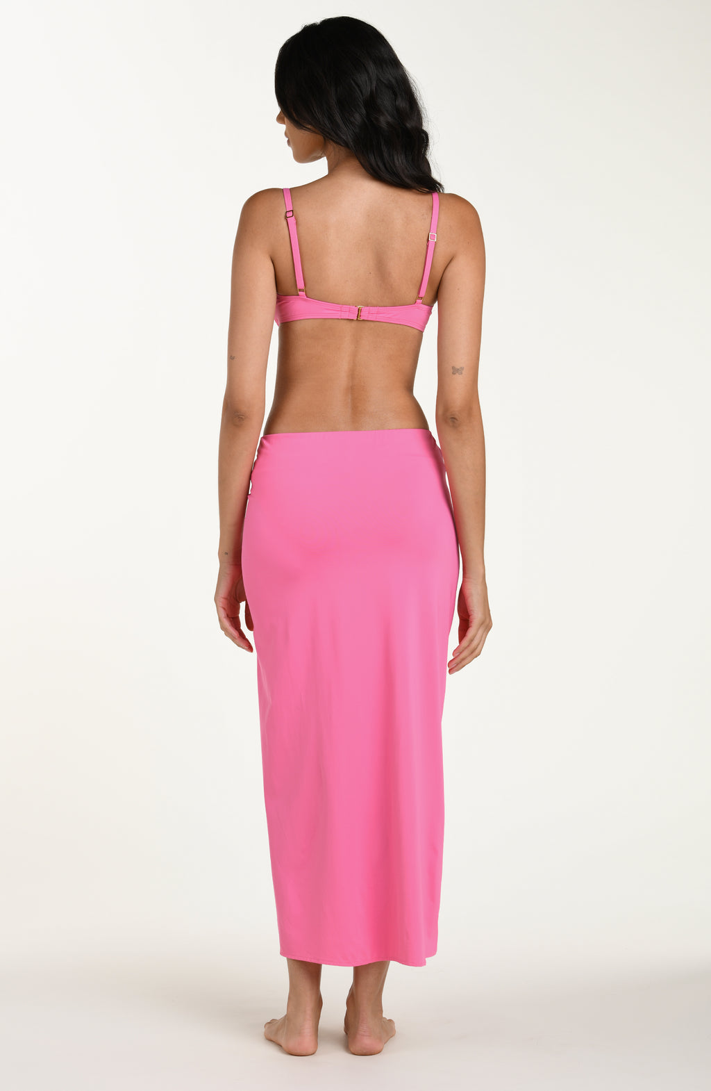 Full body back image of model wearing a rose pink colored maxi cover-up skirt with a high side slit. This is paired with a matching bikini top.