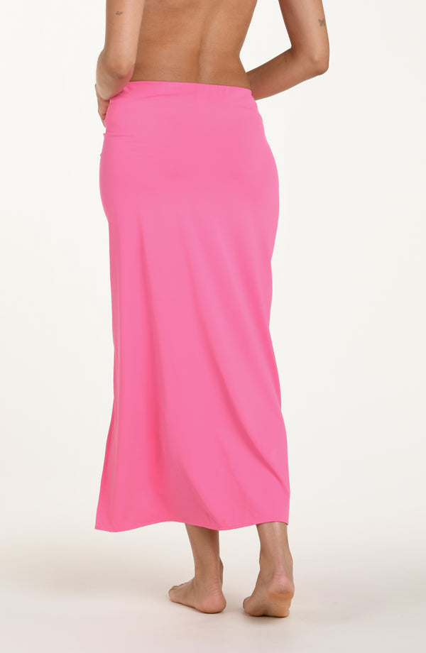 Back image of model wearing a rose pink colored maxi cover-up skirt with a high side slit. 
