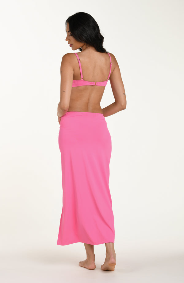 Full body back image of model wearing a rose pink colored maxi cover-up skirt with a high side slit. This is paired with a matching bikini top.