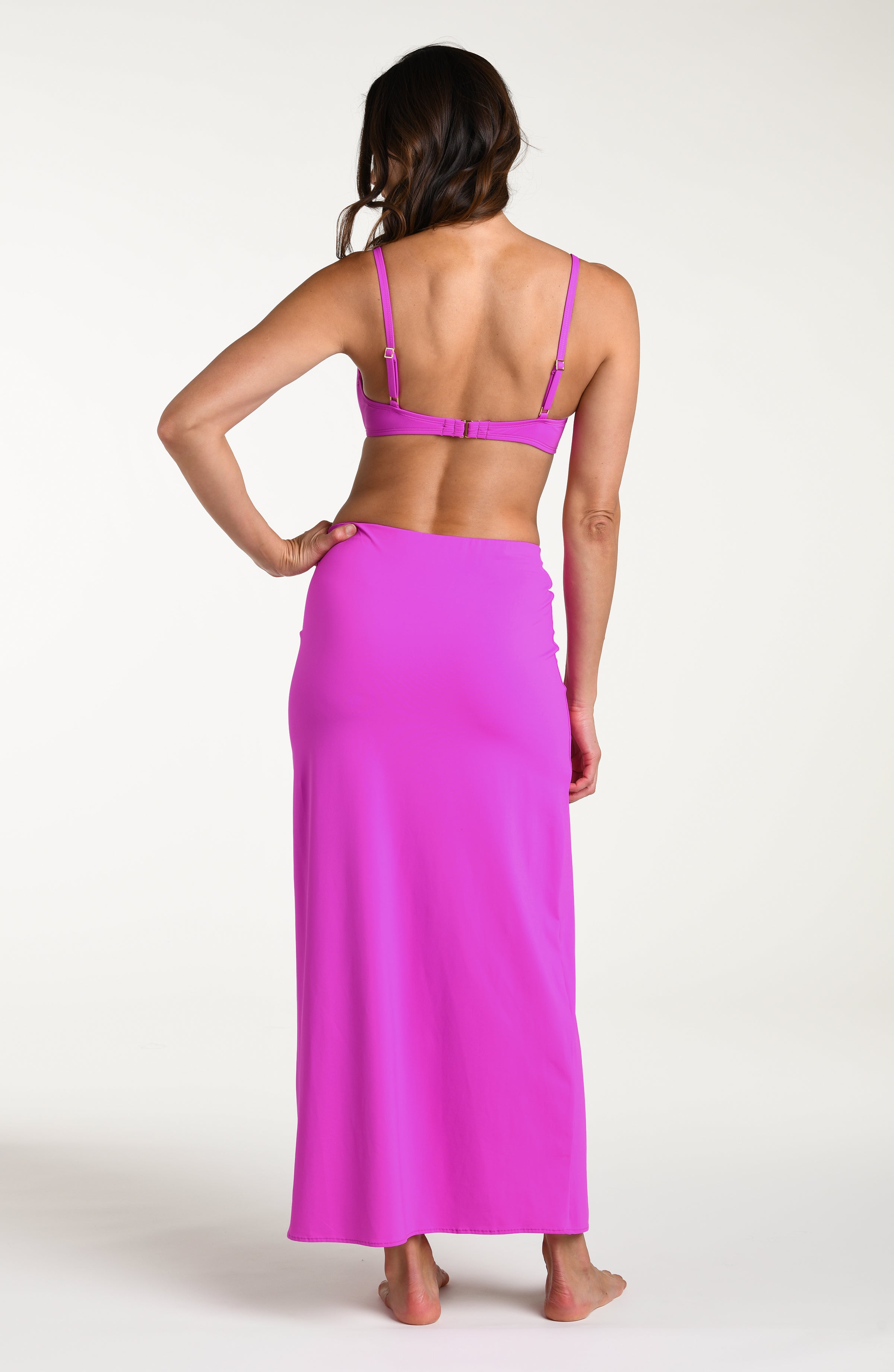 Woman wearing a violet colored bikini top and matching maxi skirt against a white background. 