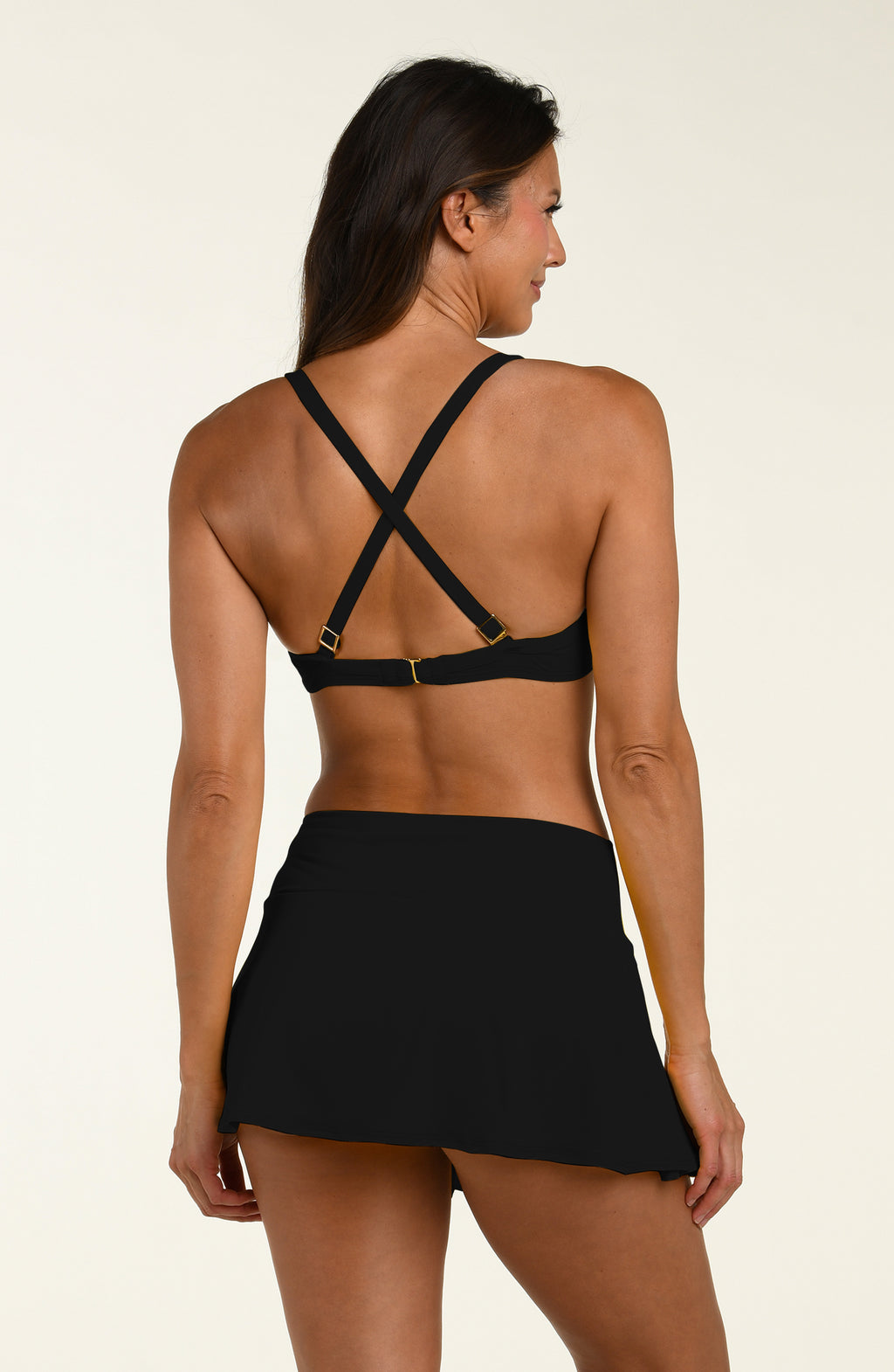 Woman wearing a black bikini top and matching swim skirt on a beige background