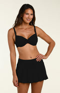 Woman wearing a black bikini top and matching swim skirt on a beige background