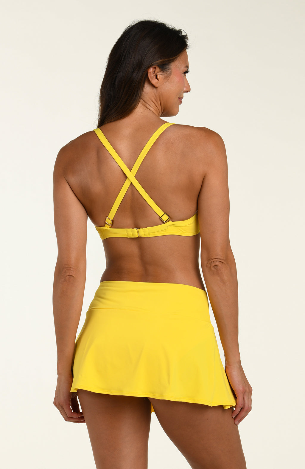 Woman wearing a yellow bikini top and a matching swim skirt bottom against a beige background.