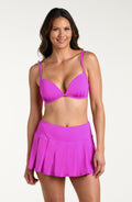 Woman wearing a violet colored bikini top and matching swim skirt against a white background.