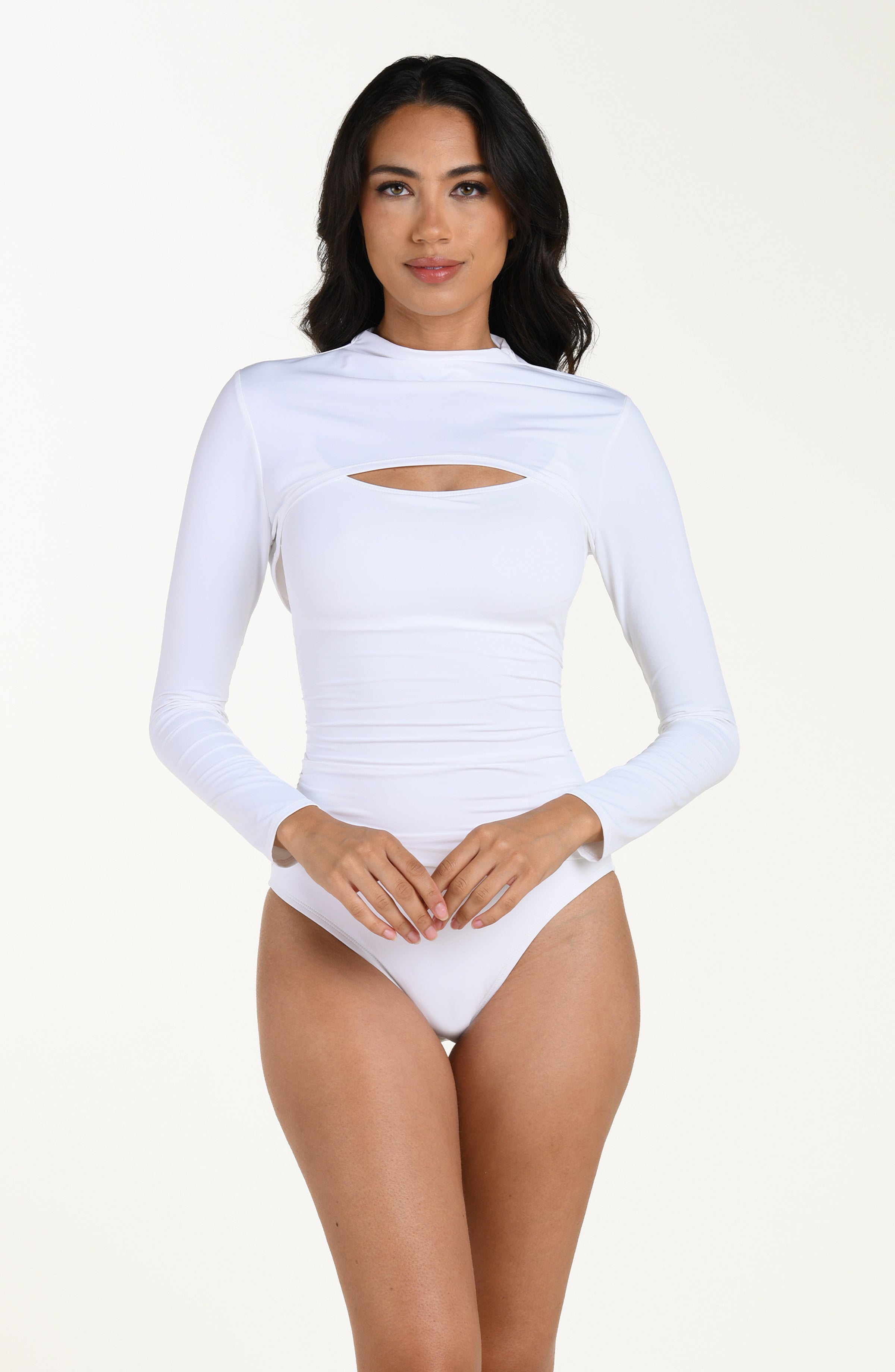 Front image of model wearing a white long-sleeve overlay top with a high neckline. This is paired with white bandeau one piece swimsuit. 