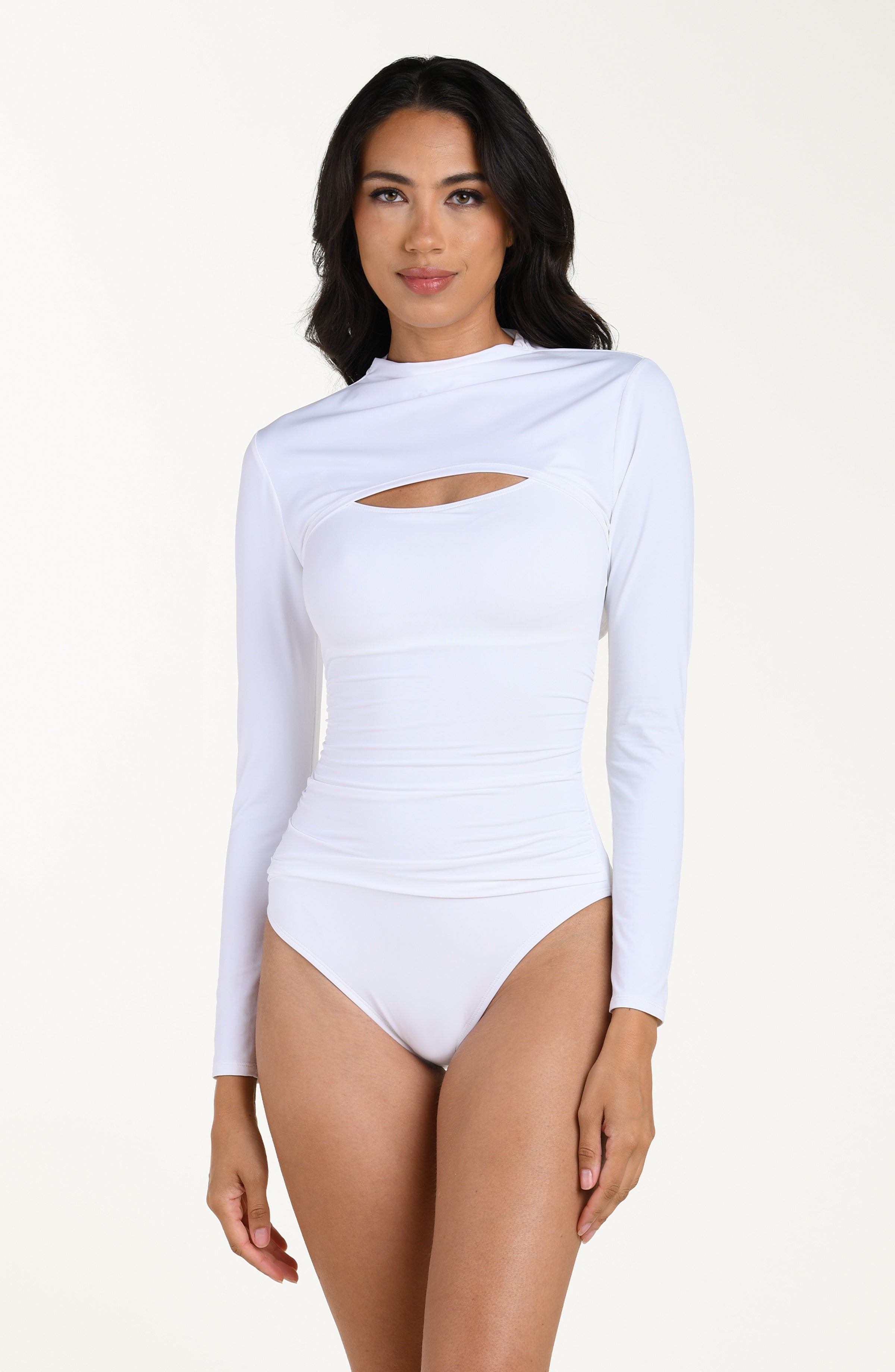 Front image of model wearing a white long-sleeve overlay top with a high neckline. This is paired with a white bandeau one piece swimsuit. 