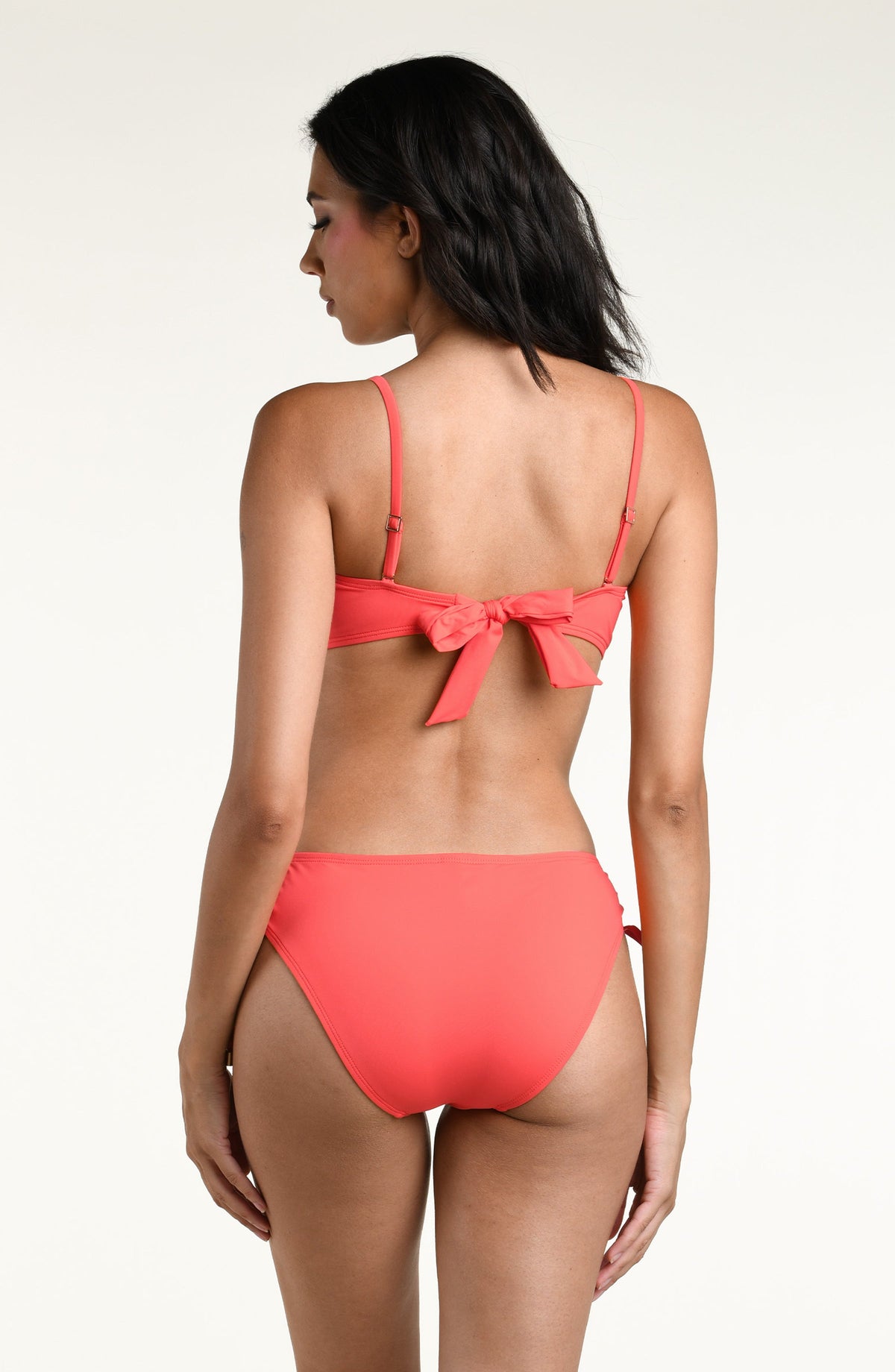 Woman wearing a bright orange bandeau bikini top and matching bikini bottom against a white background. 