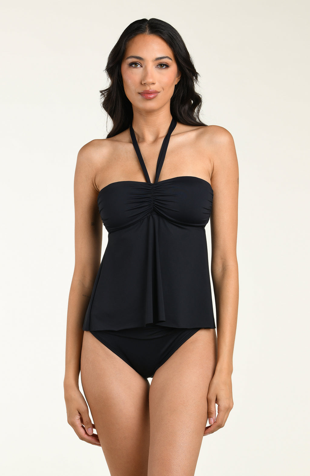 Woman wearing a black halter neck tankini top and matching bikini bottom against a beige background