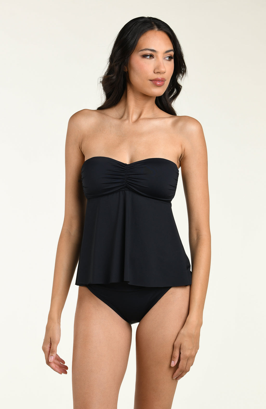 Woman wearing a black halter neck tankini top and matching bikini bottom against a beige background