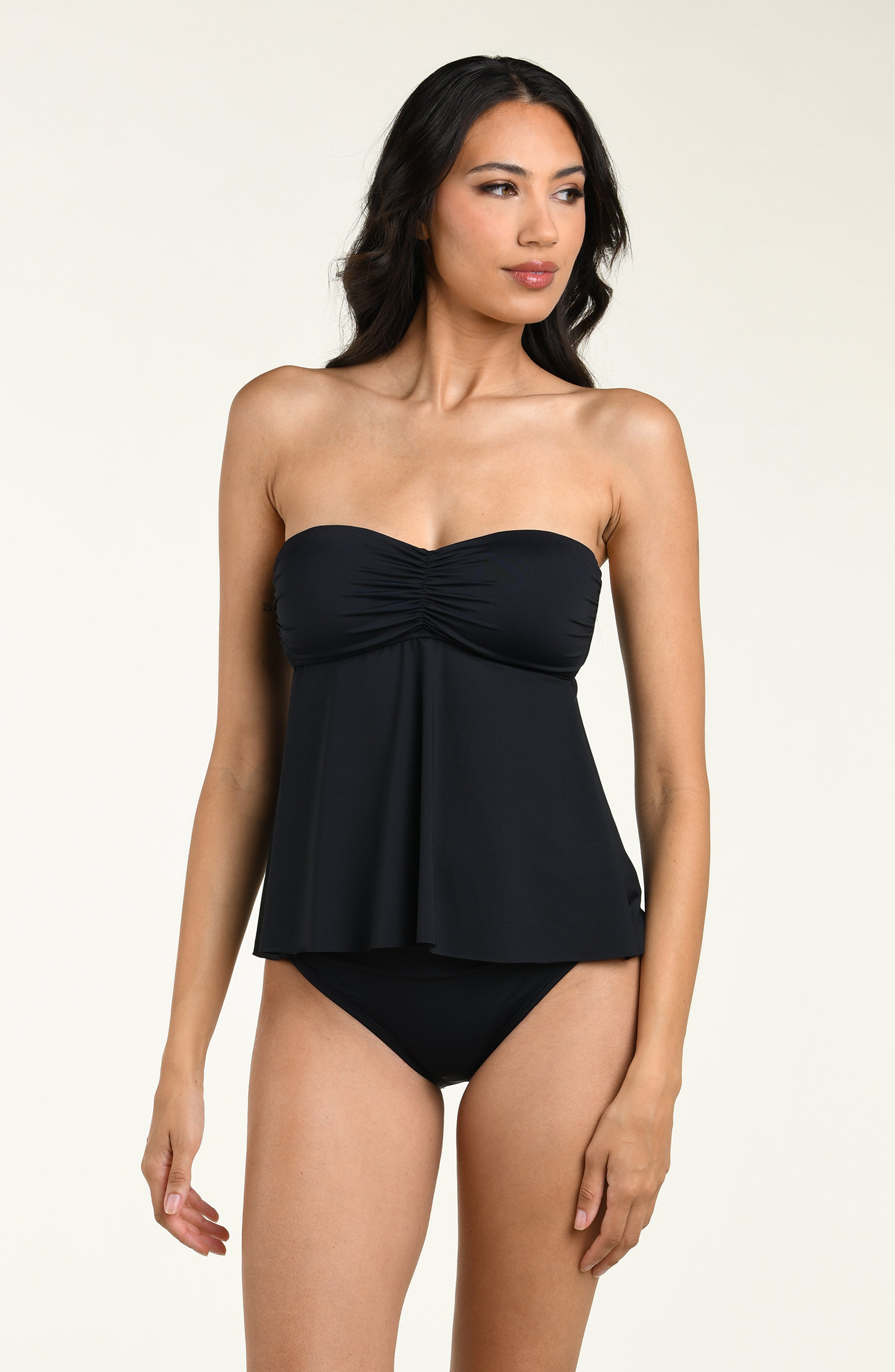 Woman wearing a black halter neck tankini top and matching bikini bottom against a beige background
