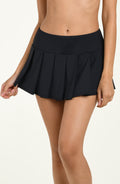 Black pleated swim skirt worn by a person on a beige background