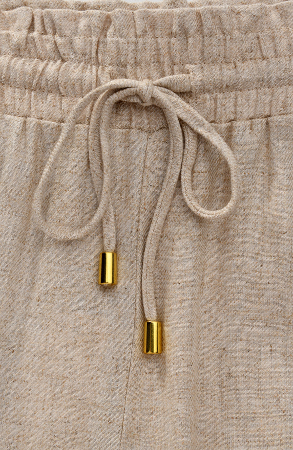 Beige pants with a drawstring and gold accents on a matching background