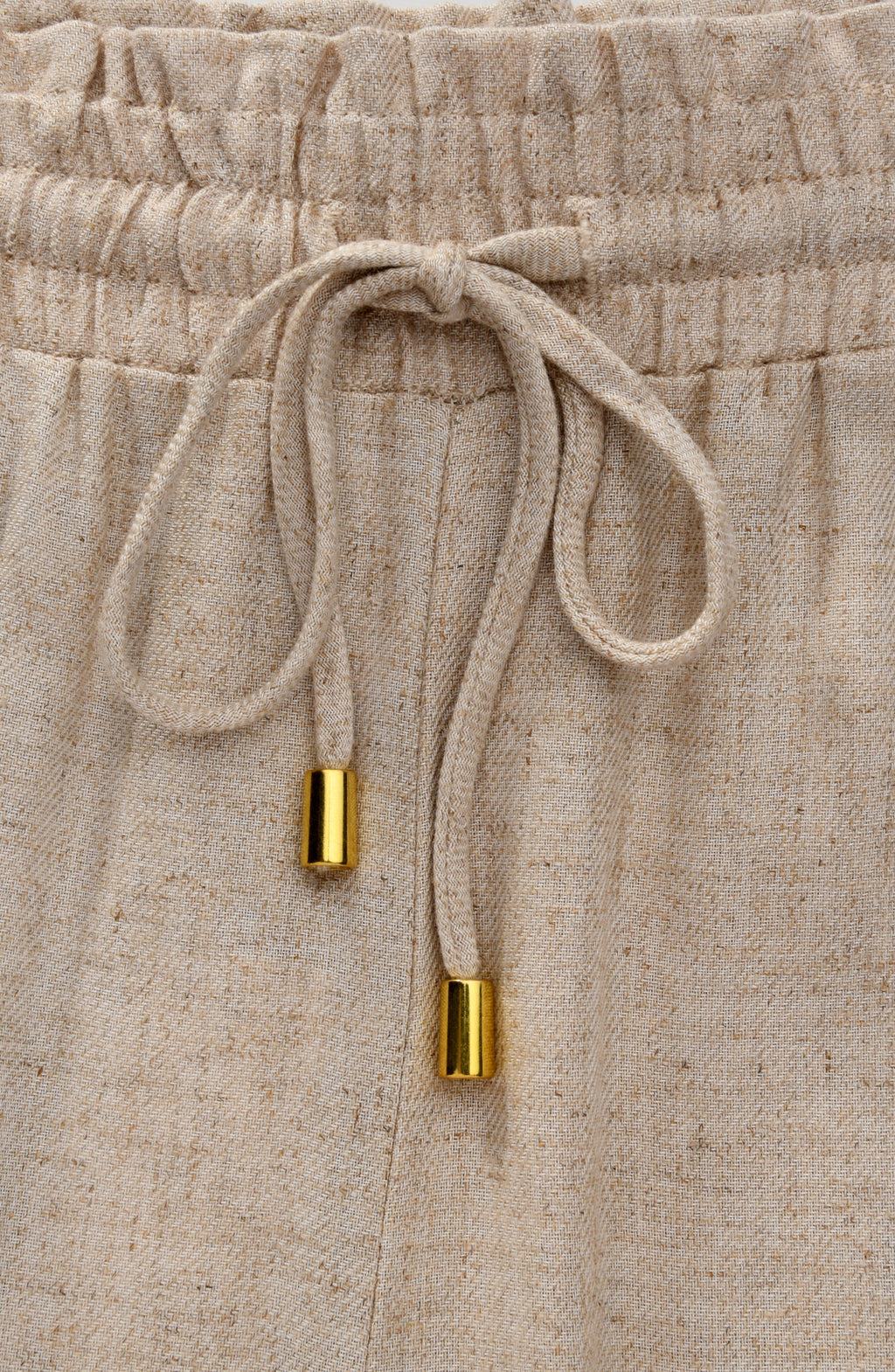 Beige pants with a drawstring and gold accents on a matching background