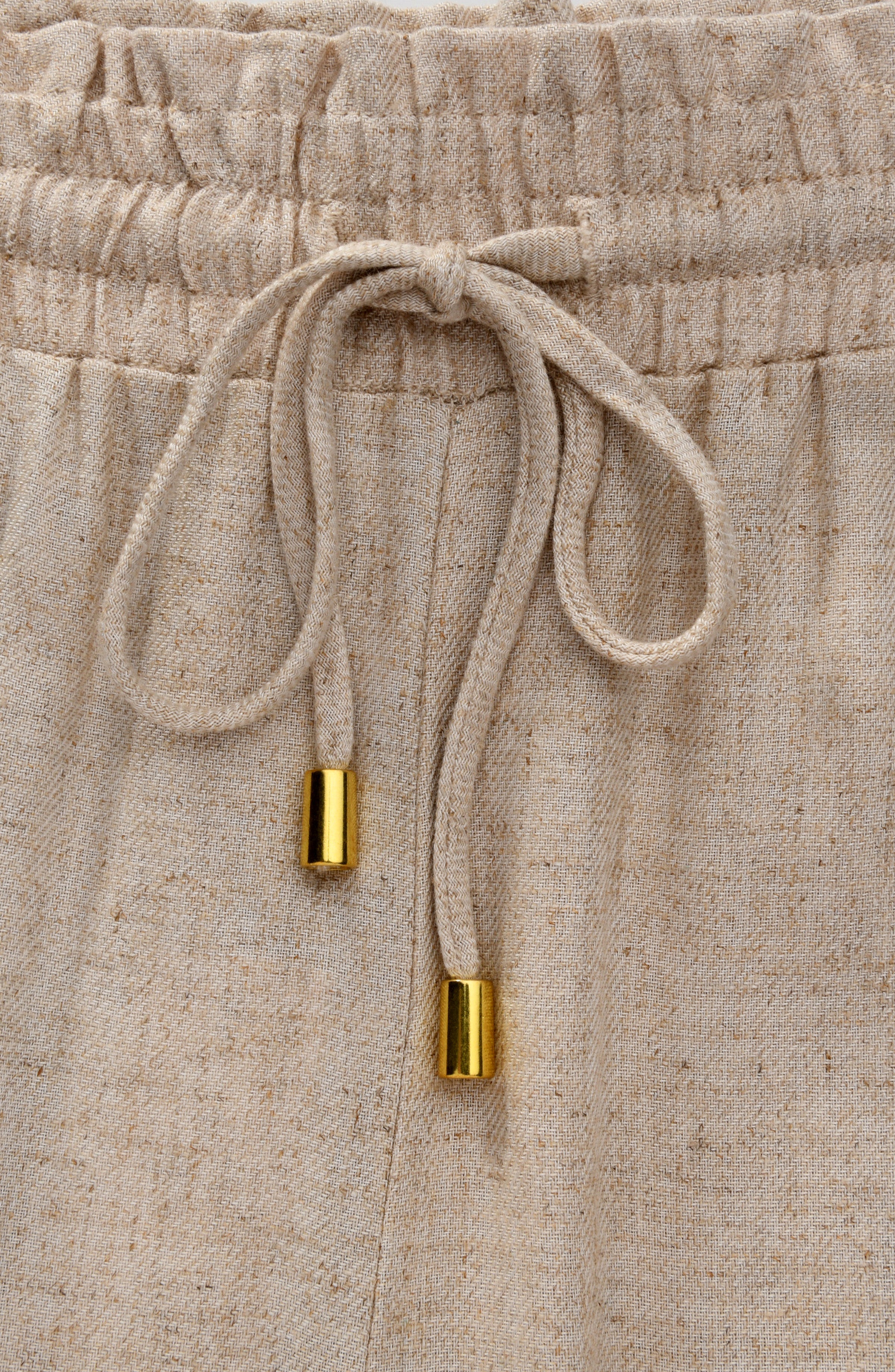 Beige pants with a drawstring and gold accents on a matching background