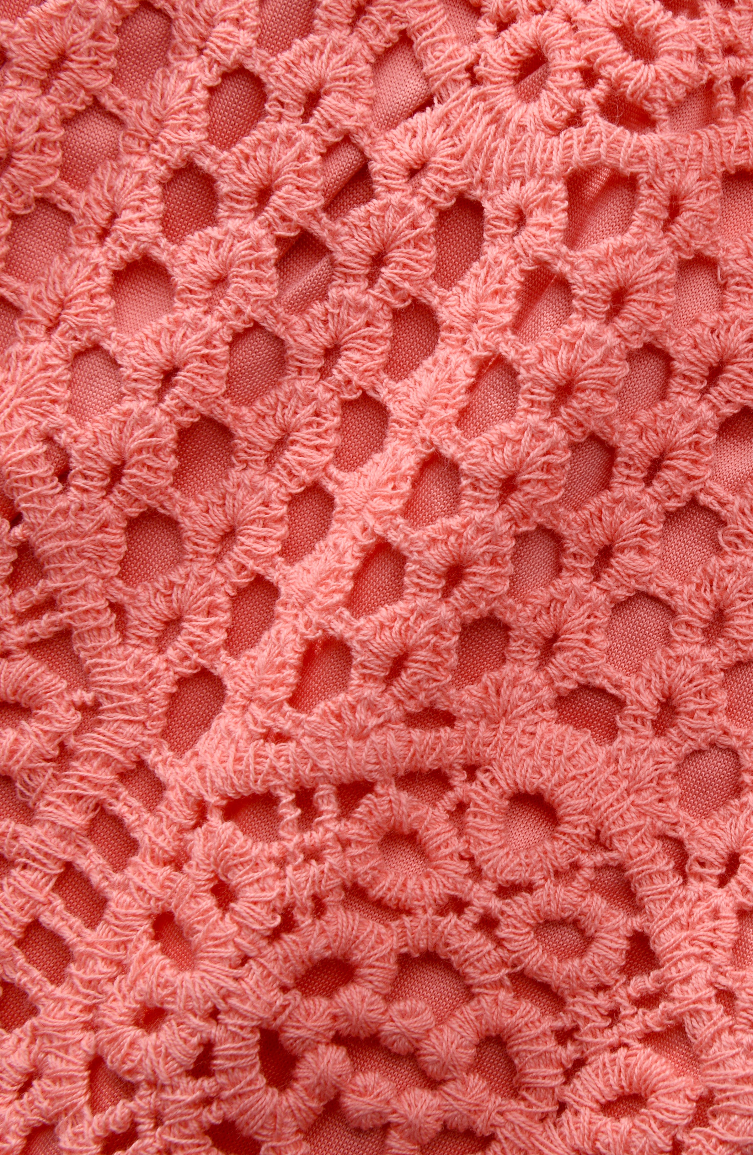 Close-up of a coral colored crochet fabric with a textured pattern