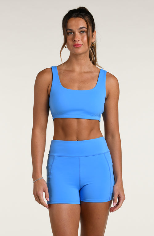 Woman wearing a blue sports bra and matching bike shorts against a white background