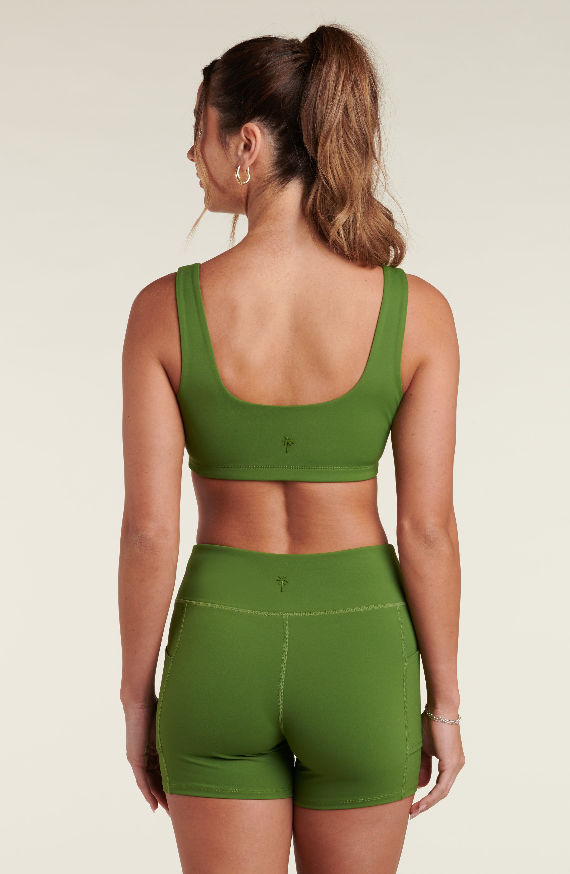 Woman wearing a green sports bra and matching biker shorts against a white background.