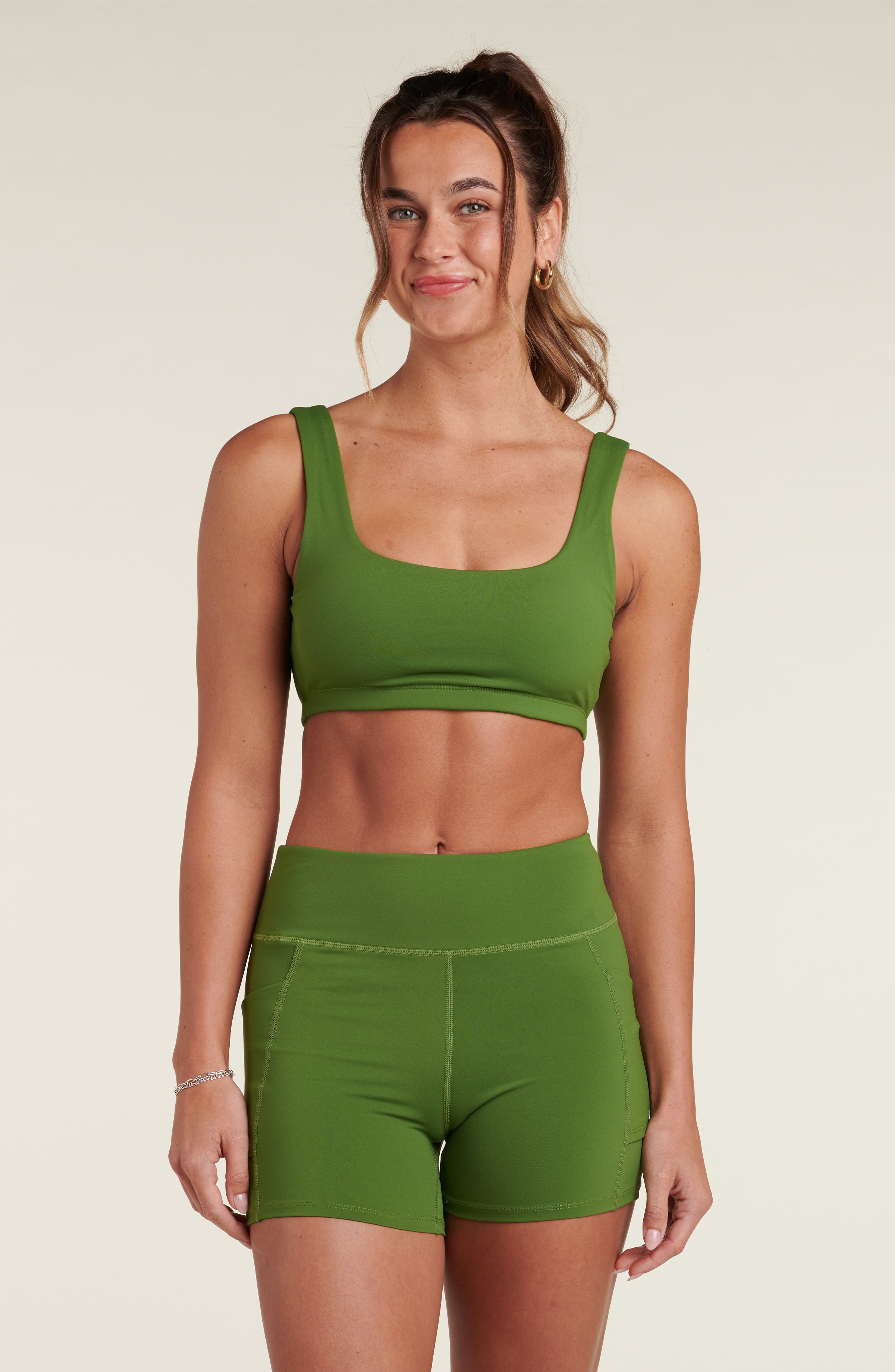 Woman wearing a green sports bra and matching biker shorts against a white background. 