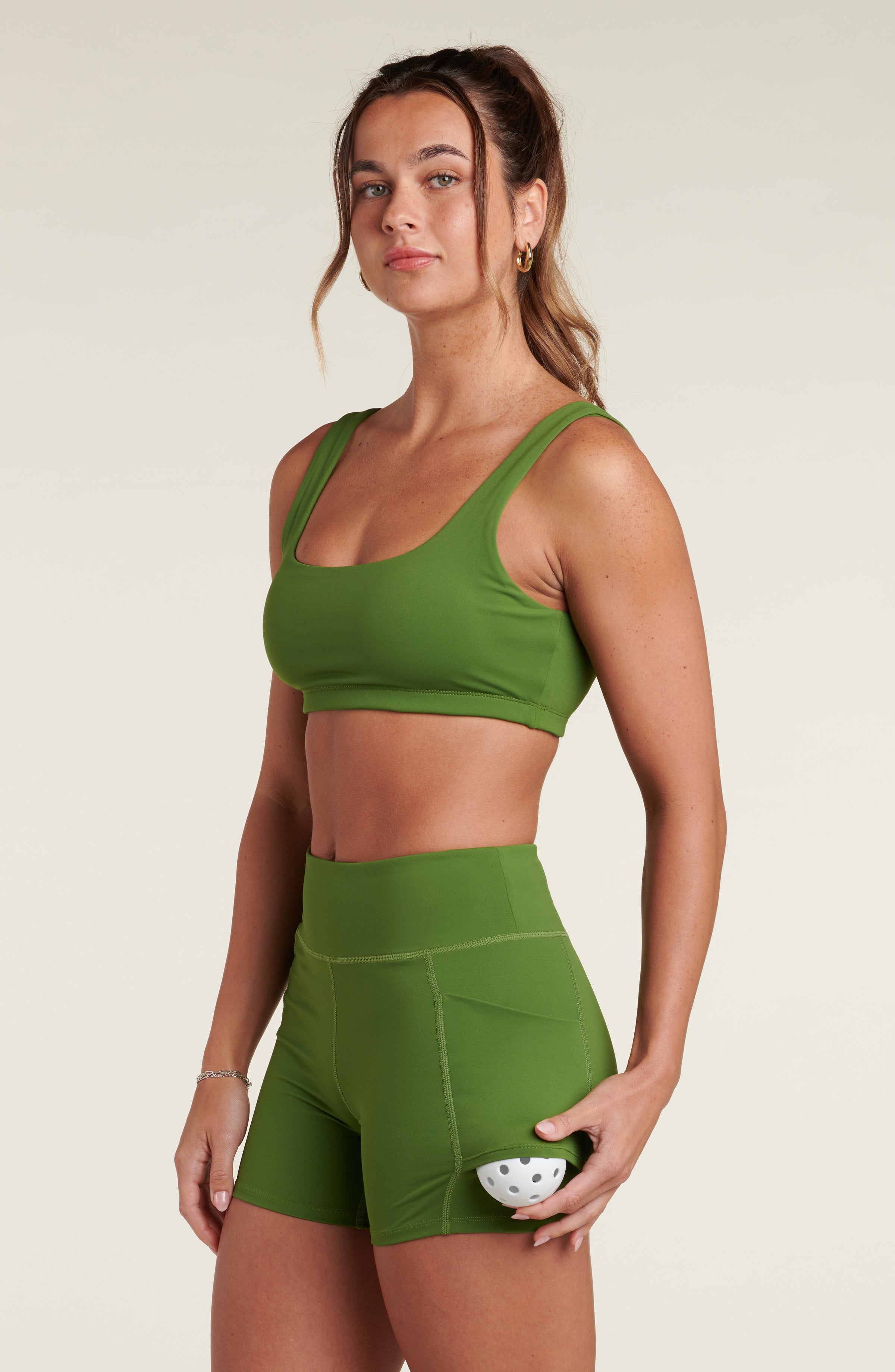 Woman wearing a green sports bra and matching biker shorts against a white background.