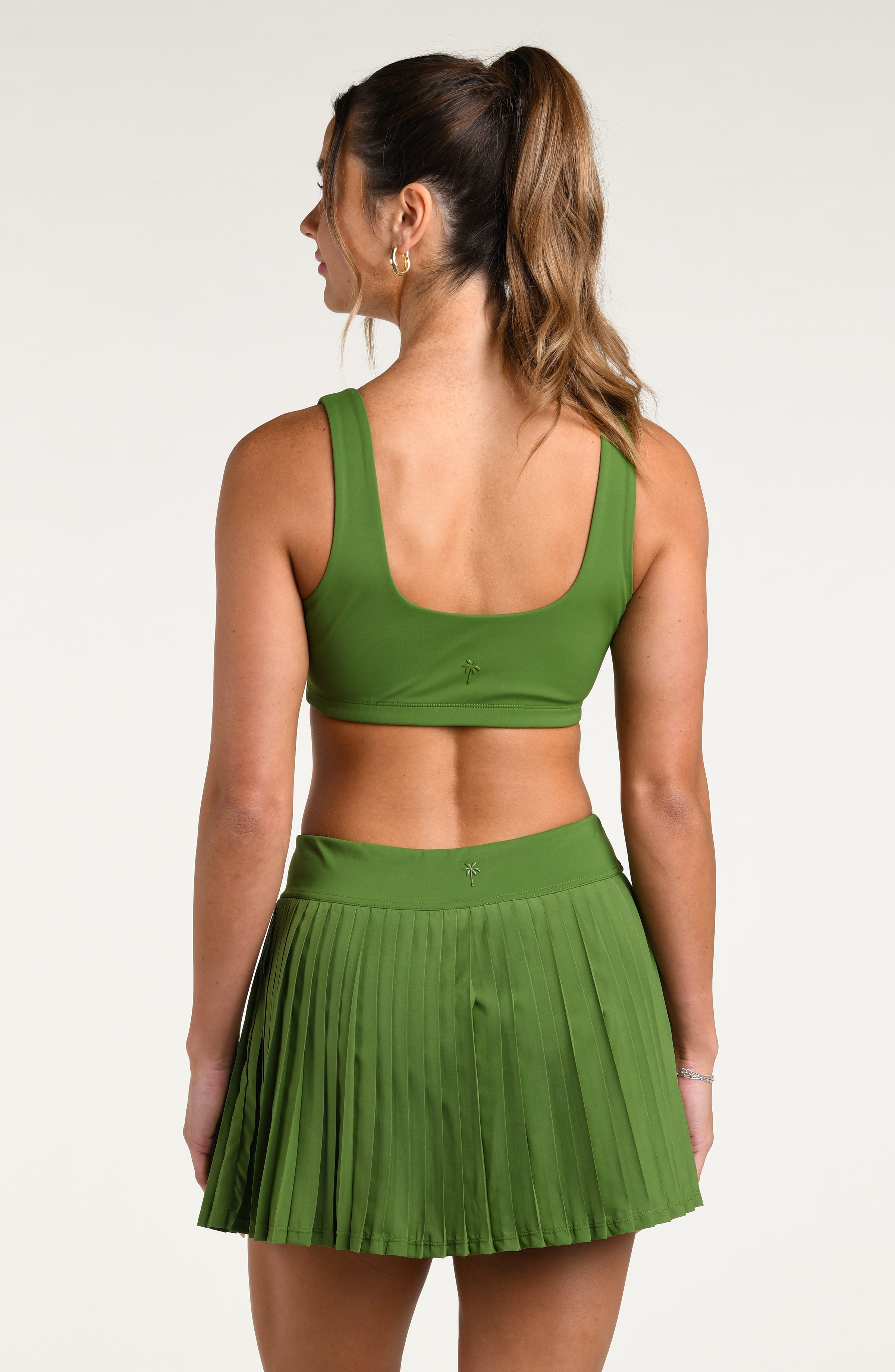 Woman wearing a green sports bra and matching swim skort against a white background