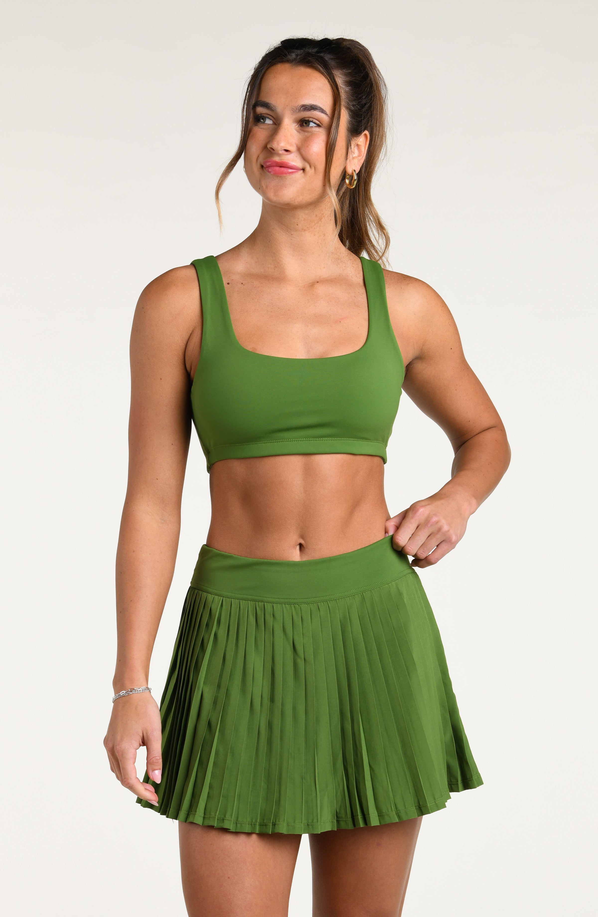 Woman wearing a green sports bra and matching skort against a white background.