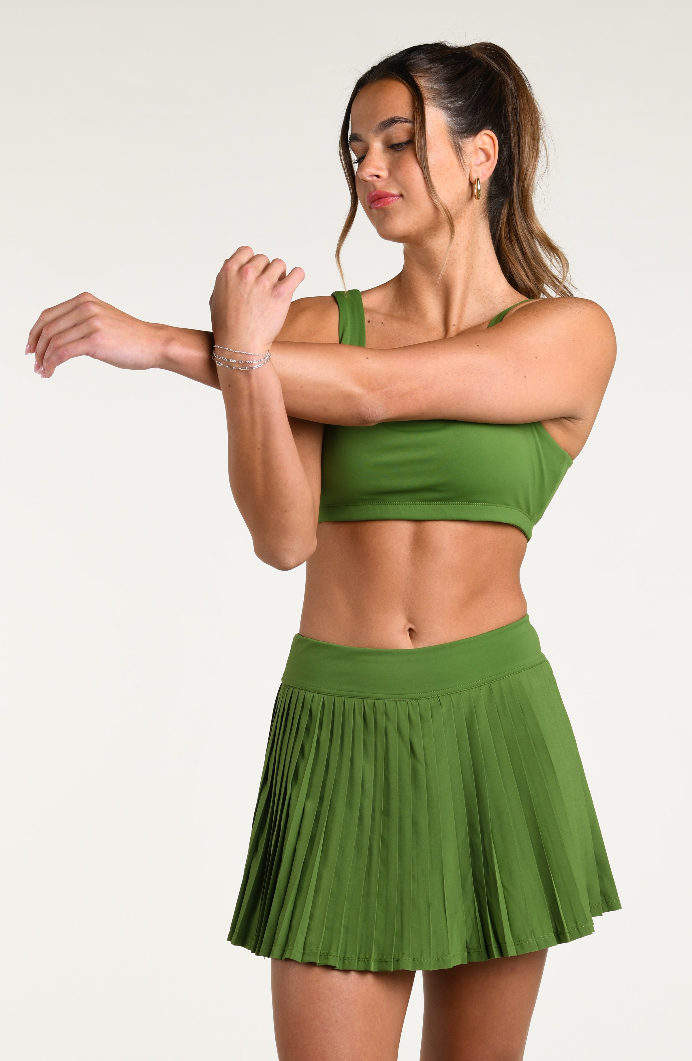 Woman wearing a green sports bra and matching skort bottom against a white background.