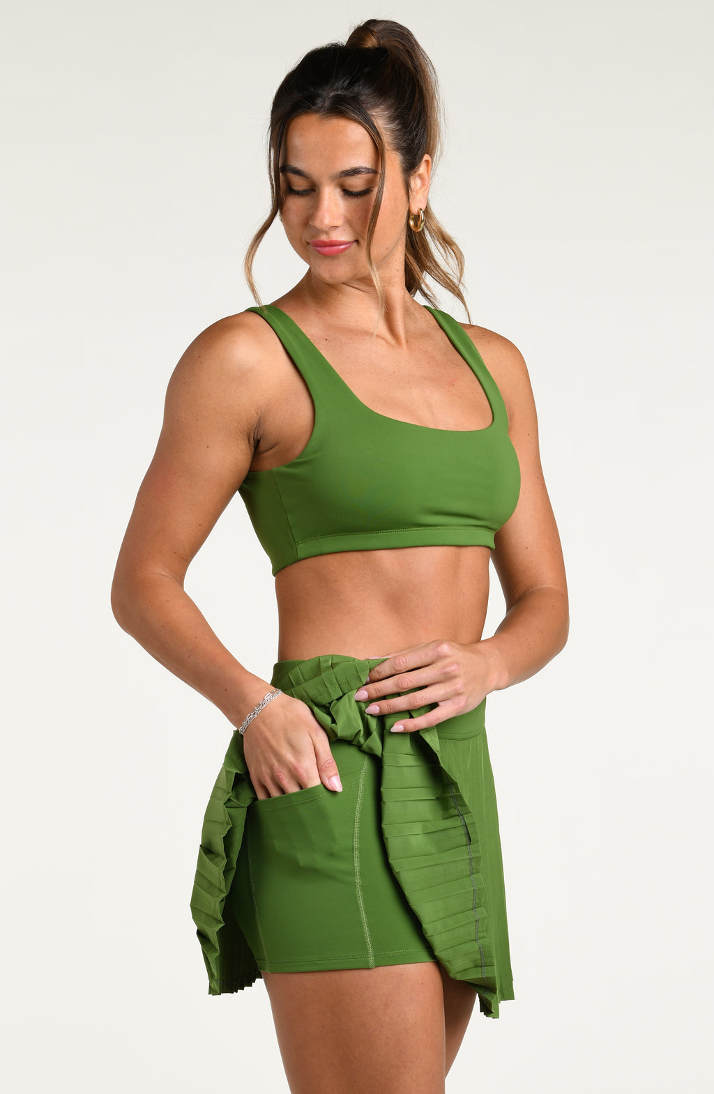 Woman wearing a green sports bra and matching swim skort against a white background