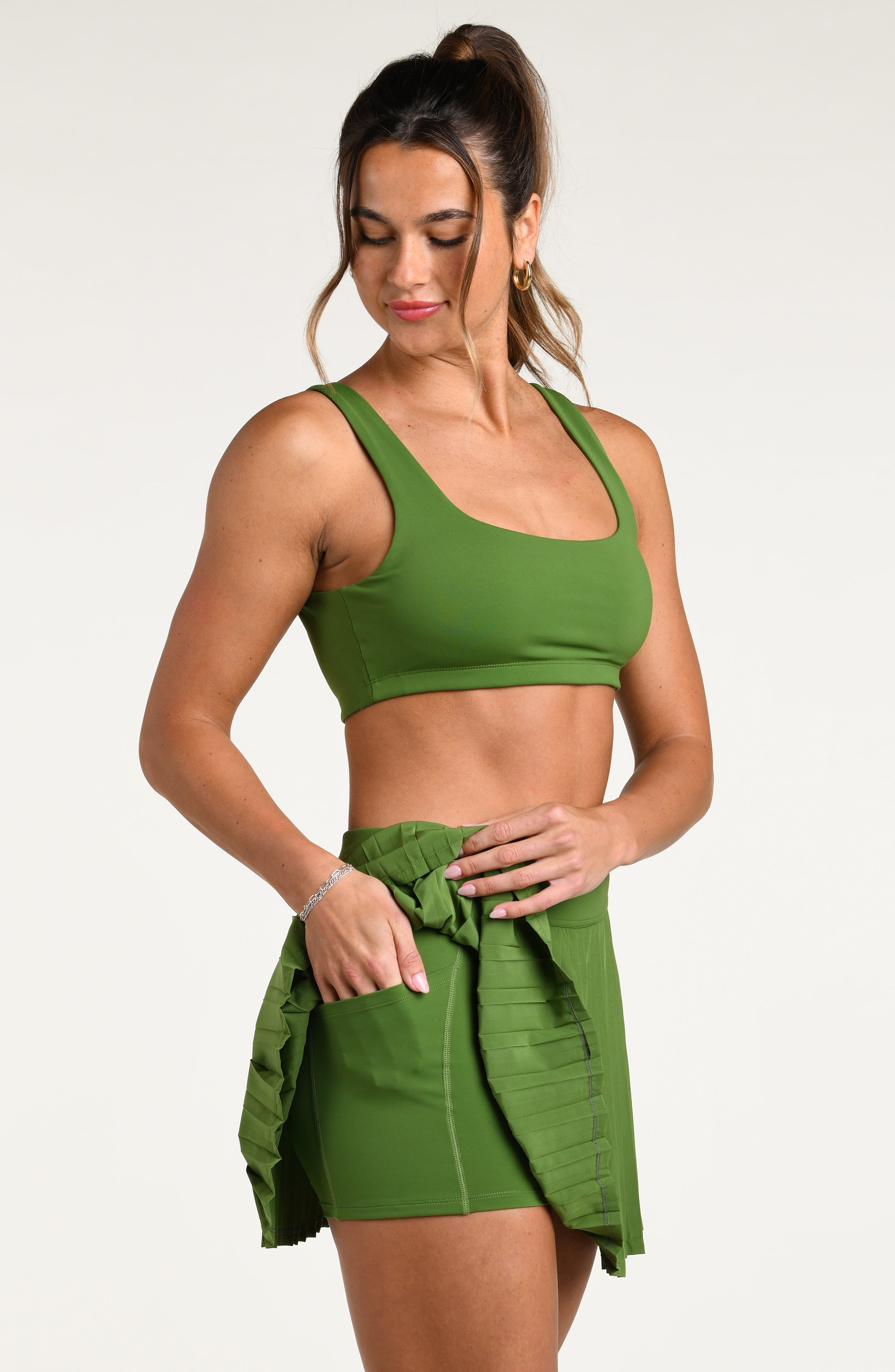 Woman wearing a green sports bra and matching swim skort against a white background