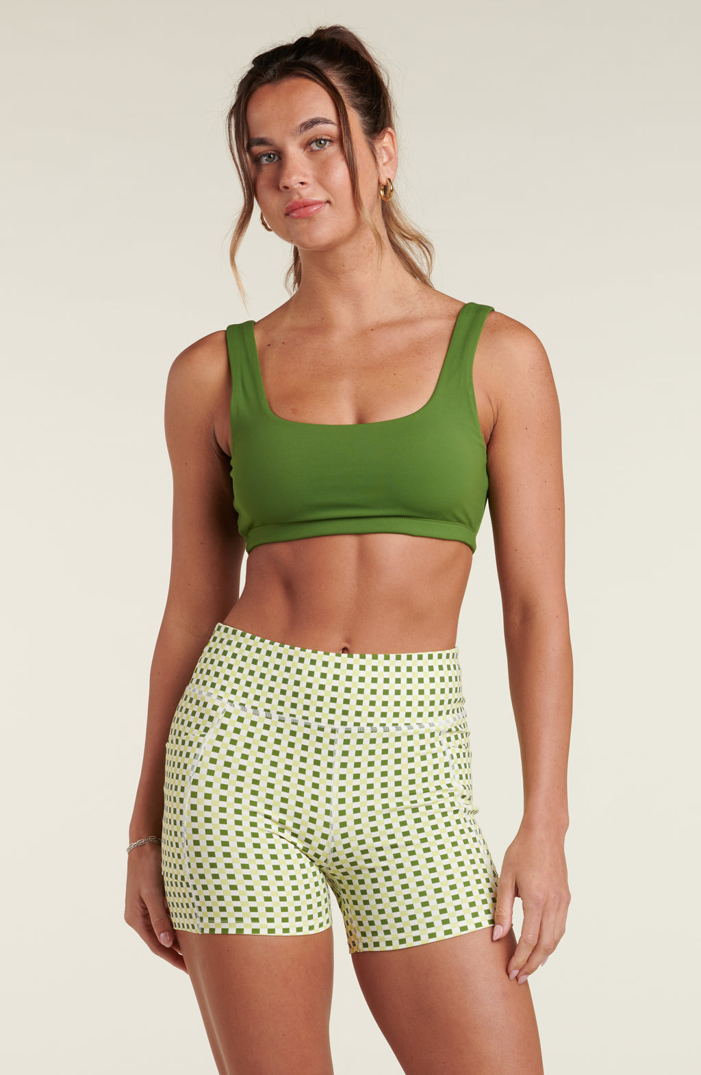 Woman wearing a green sports bra and a green and white multicolored biker skort against a white background