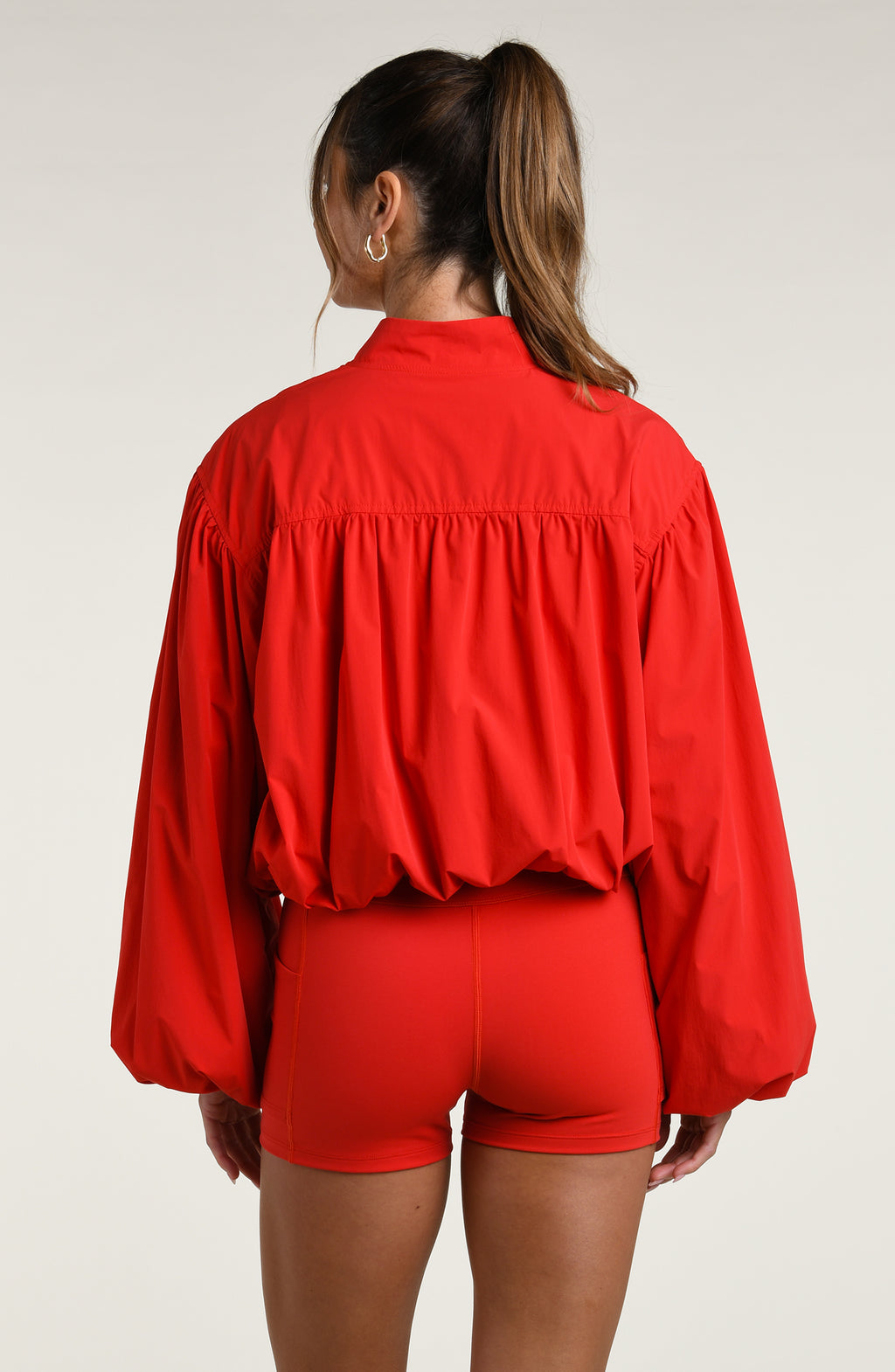Woman wearing red sports bra and matching bike shorts with a jacket, against a white background