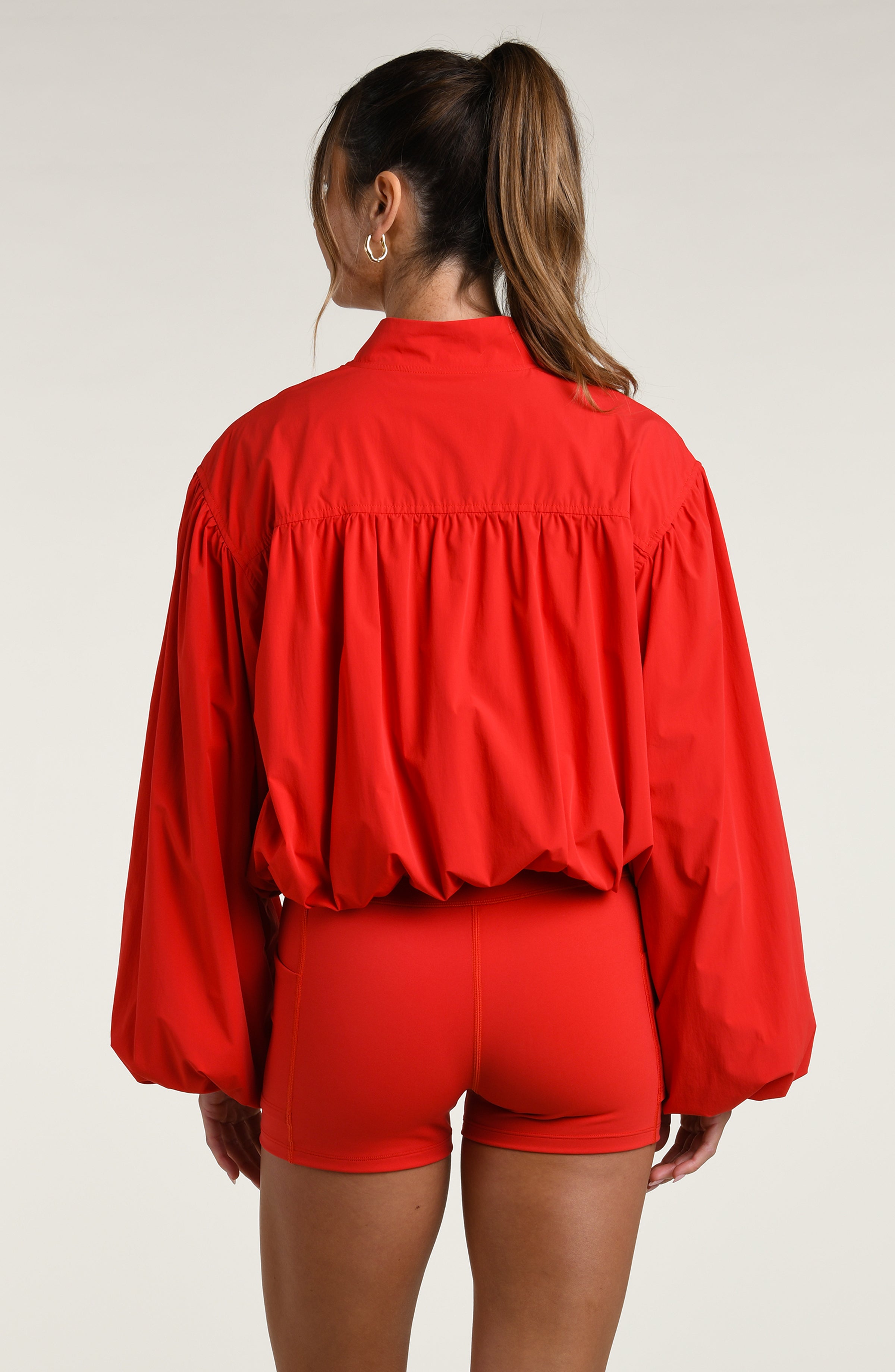Woman wearing red sports bra and matching bike shorts with a jacket, against a white background