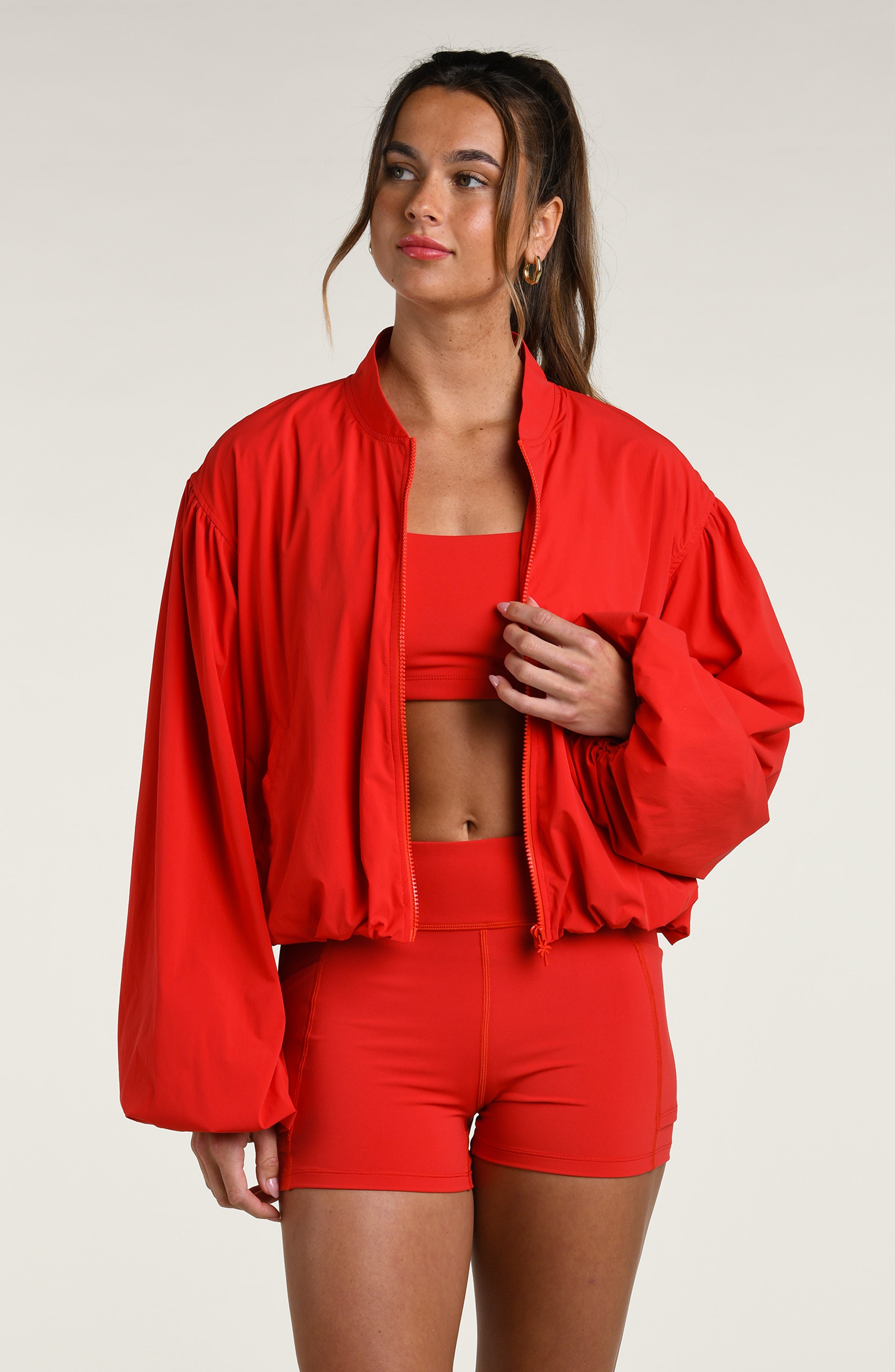 Woman wearing a red athletic jacket over a red sports bra and matching bike shorts against a white background