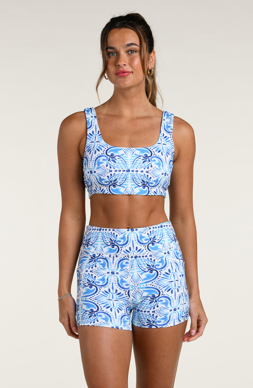 Woman wearing a blue and white multicolored patterned sports bra and matching bike shorts worn by a person on a beige background